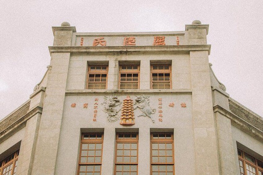 Een gebouw met een traditionele architectuur, met een opvallende standbeeld van een leeuw bij de ingang, grote ramen en decoratieve details. 3