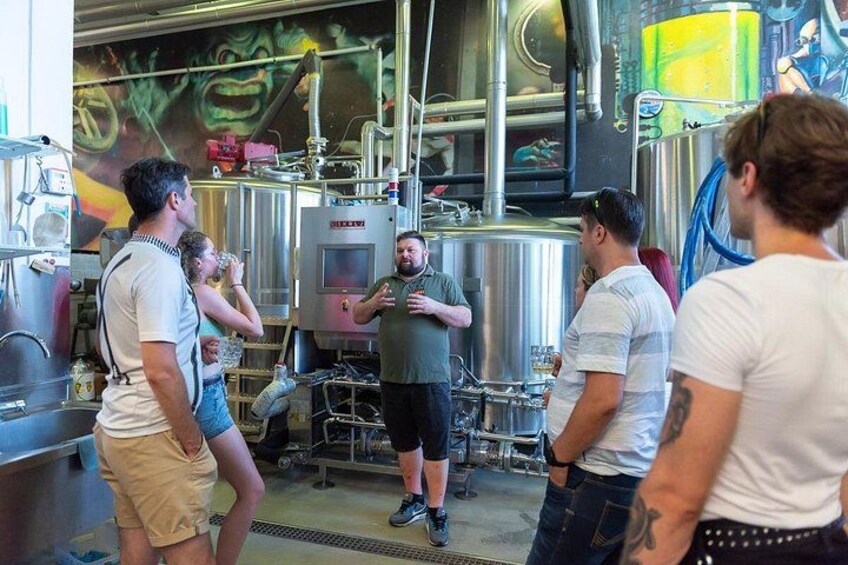 Un grupo de personas en una cervecería, con tanques de acero inoxidable y equipo de elaboración. 4