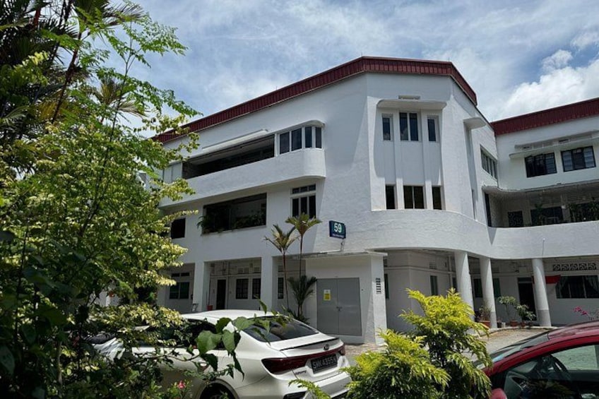 A white multi-story building with a red roof, parked cars, and lush greenery. 2