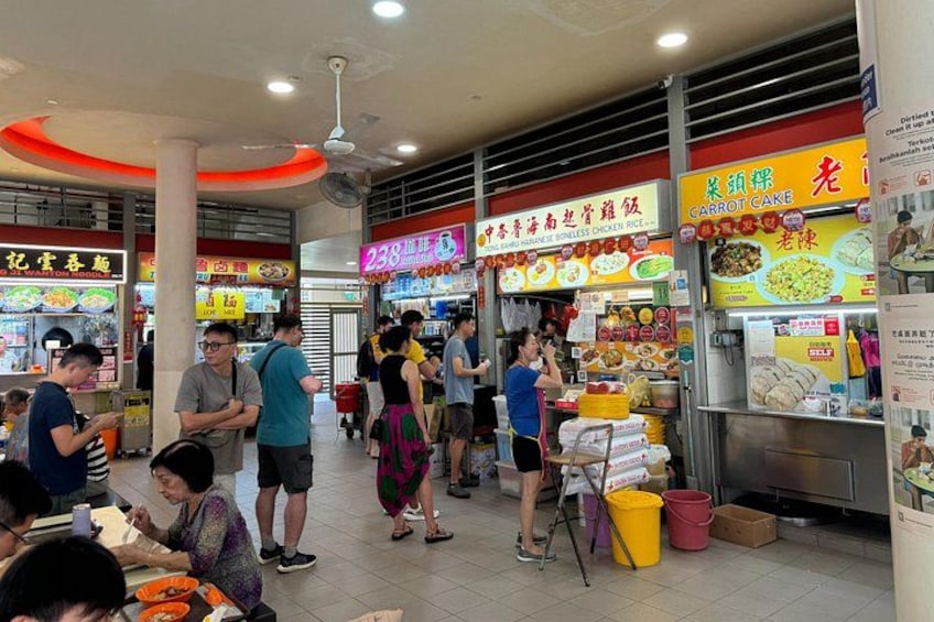 A bustling indoor food court with multiple food stalls, people dining and standing around. 4