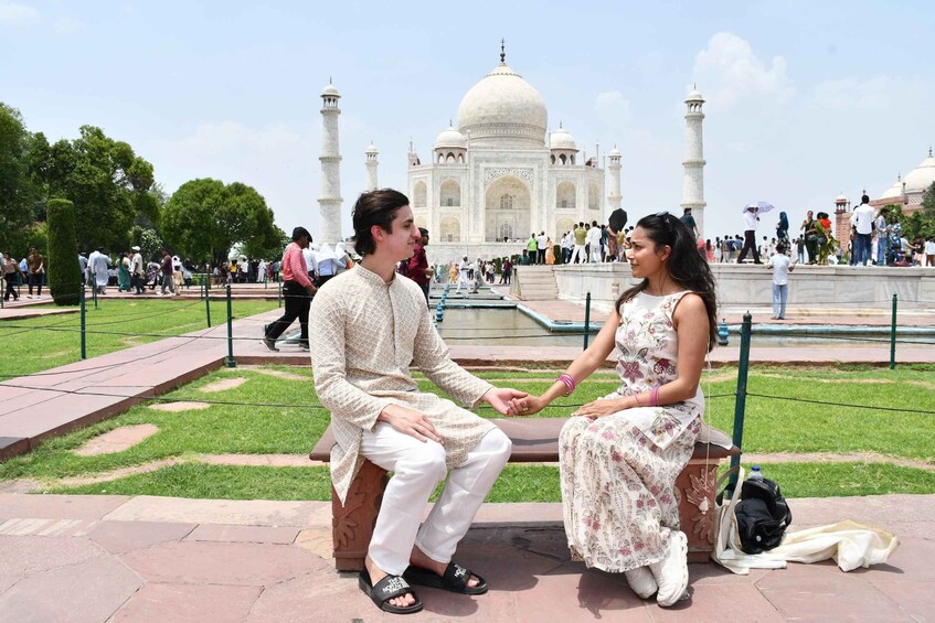 Two people sitting on a bench in front of the Taj Mahal, with a crowd in the background. 1