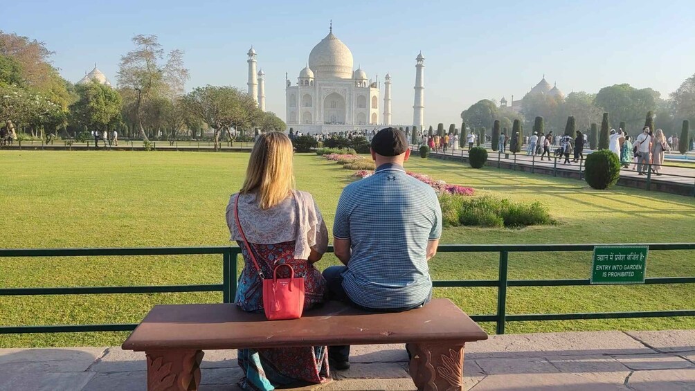 A couple sitting on a bench facing the Taj Mahal. 2