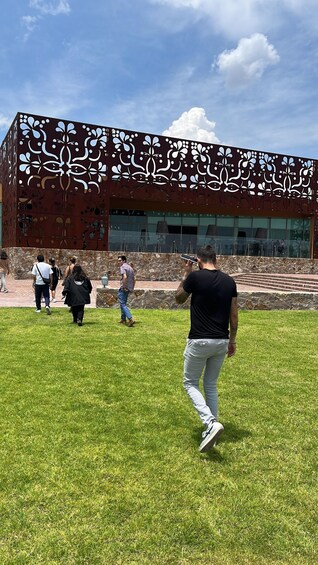 A modern building with a unique facade featuring geometric patterns, a grassy area in front, and a clear blue sky. 4