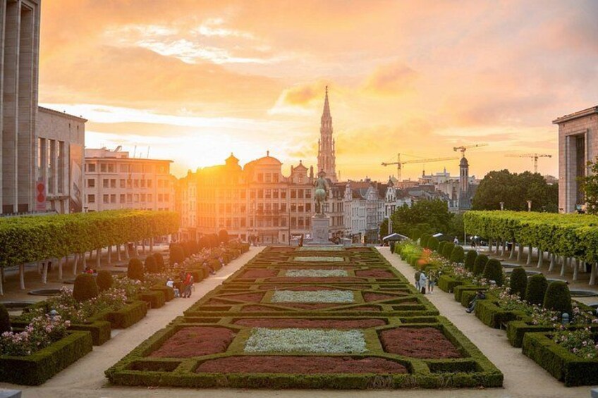 A formal garden with geometric patterns, a central fountain, and historic buildings in the background. 3