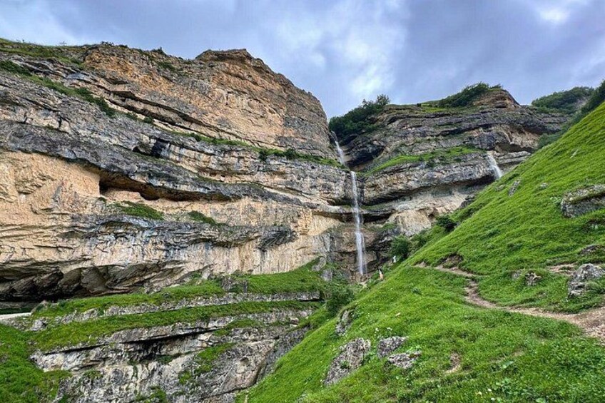 A waterfall cascading down a rocky cliff with layered rock formations and green vegetation. 1