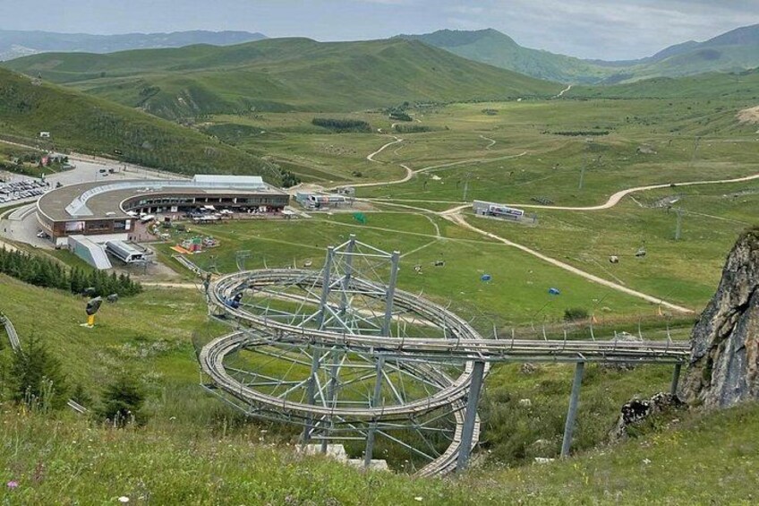 A mountainous landscape with a winding road, a large building, and a complex railway interchange. 3