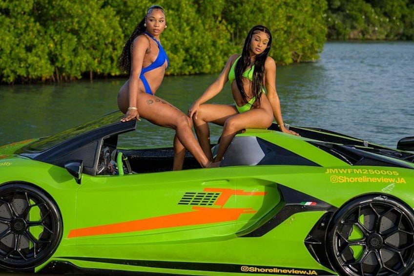 Un coche deportivo verde brillante con dos mujeres sentadas encima, rodeado de agua y vegetación. 2