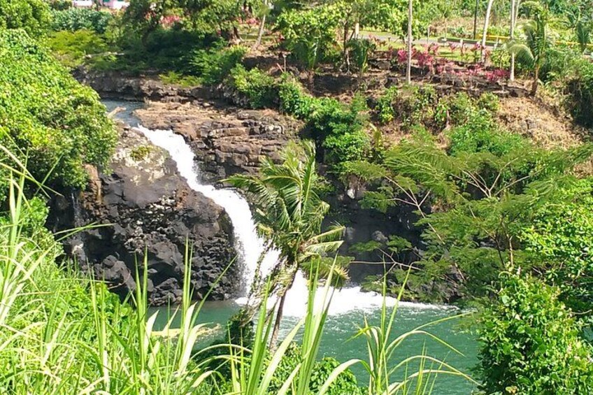 Una cascada fluye sobre rocas, rodeada de exuberante vegetación y un cuerpo de agua azul y cristalino. 2