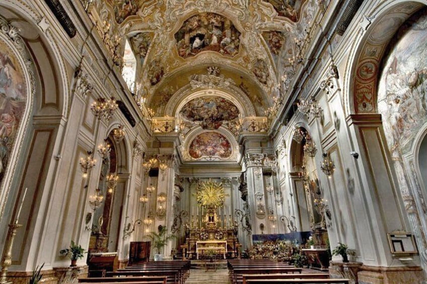 An ornate church interior with detailed frescoes, a central altar, and rows of pews. 2