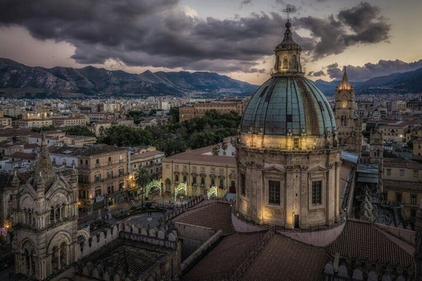 A cityscape with a prominent dome and surrounding architecture, mountains in the background, and a cloudy sky. 2