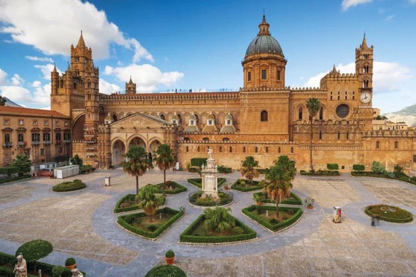 Un edificio histórico con una gran cúpula y torres de campanas, rodeado de un jardín cuidado con estatuas. 3