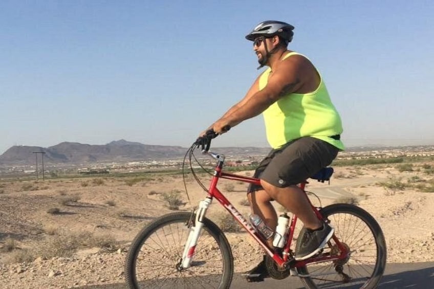 A person riding a red bicycle on a dirt road with a desert landscape in the background. 2