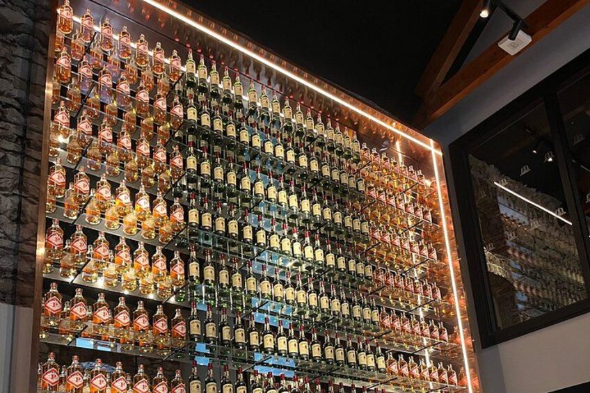 Una pared con varias botellas de licores, dispuestas en filas ordenadas e iluminadas por luces. 2