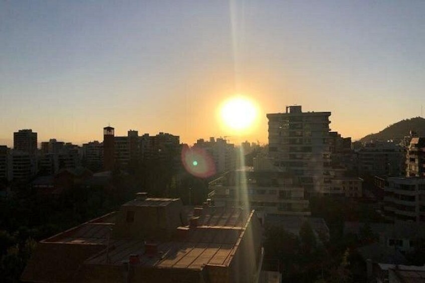 A cityscape at sunset with the sun low on the horizon, casting a glow over buildings and rooftops. 3