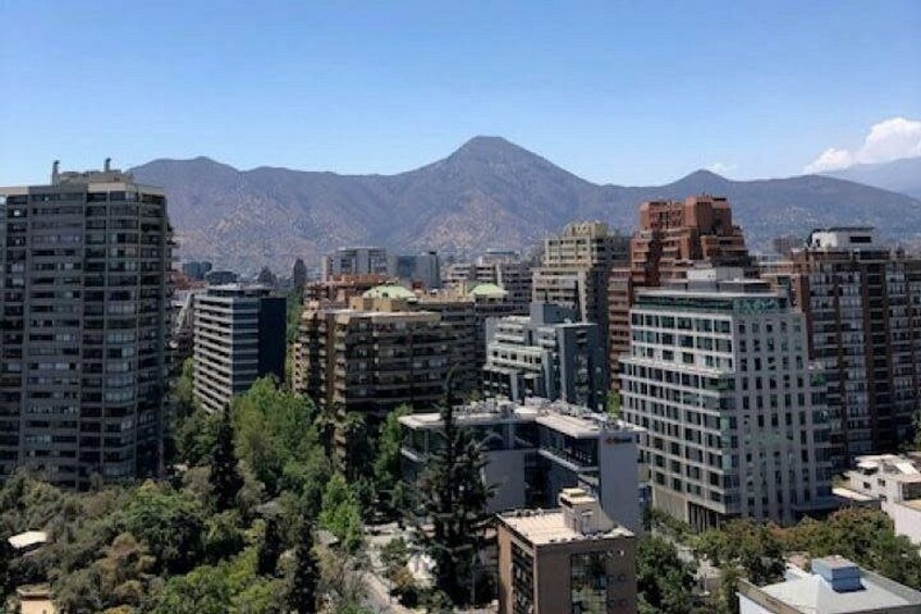 A cityscape with high-rise buildings, a mountain range in the background, and some greenery in the foreground. 1