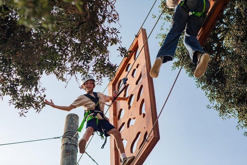 A person zip-lining with a safety harness, a wooden zip line structure, and trees in the background. 4