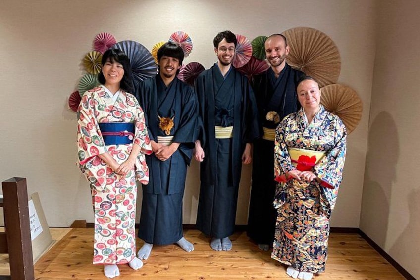 Un groupe de personnes vêtues de costumes traditionnels japonais, debout à l’intérieur, tenant des éventails et se tenant sur un plancher en bois. 3
