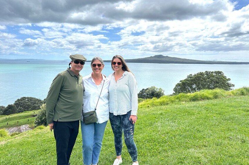 Three people standing on a grassy hill with a lake and mountains in the background. 4