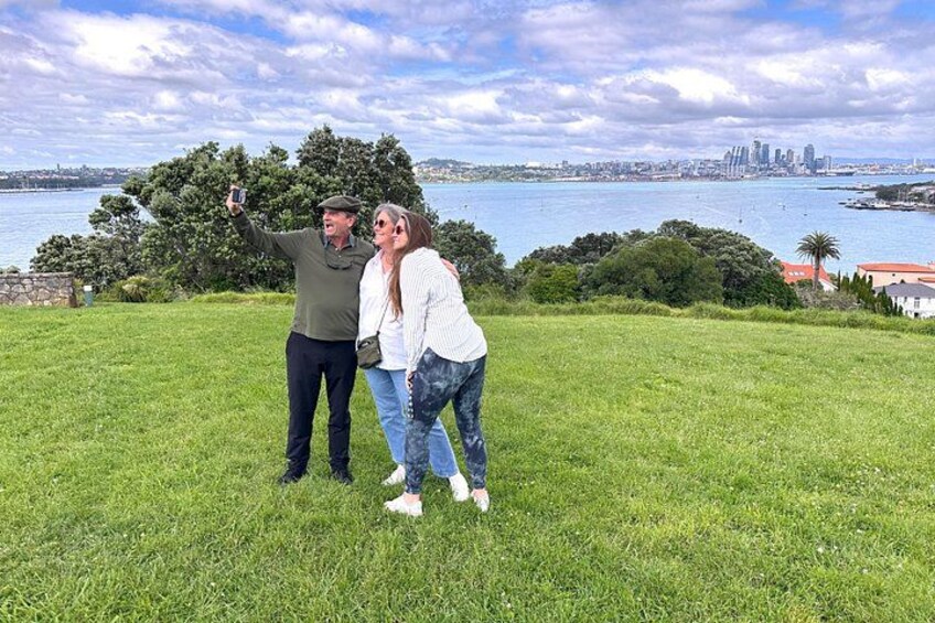 A couple taking a selfie on a grassy hill with a city skyline in the background. 3