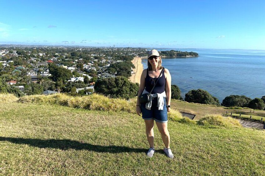 A person standing on a grassy hill overlooking a coastal town with houses and a body of water. 4