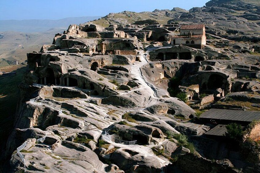Un paisaje agreste con antiguas formaciones rocosas y un pequeño edificio en una colina. 4