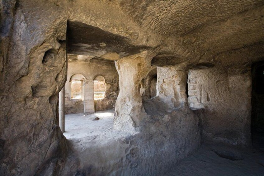 Interior de una cueva con formaciones rocosas naturales, un pilar central y aberturas en arco. 3