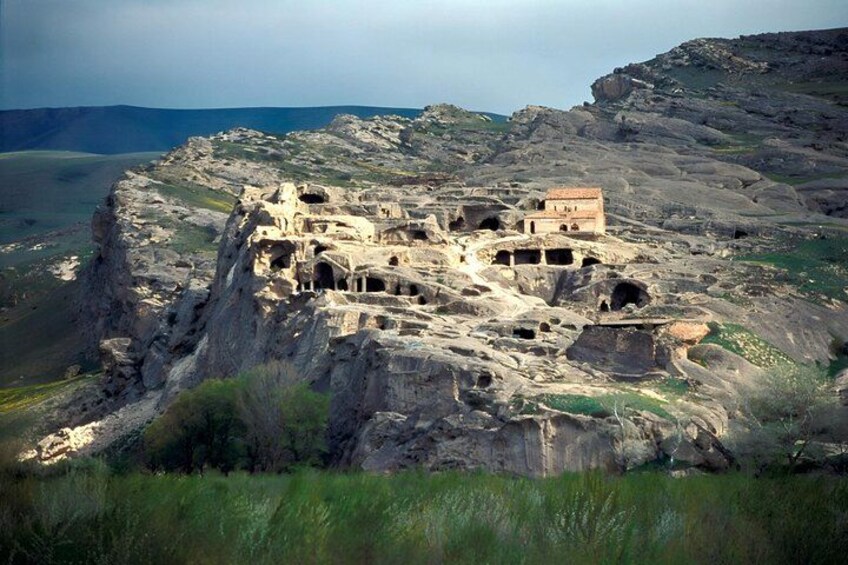 Una estructura excavada en la roca con varios niveles y un pequeño edificio en la parte superior. 5