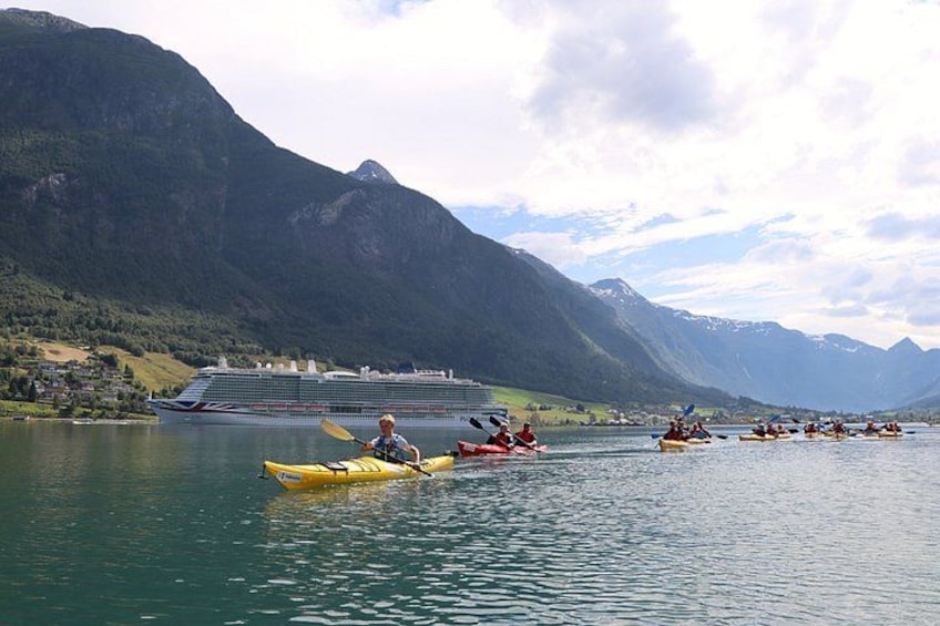 Un grupo de kayakistas en un lago tranquilo con montañas al fondo y un crucero amarrado en la orilla. 3