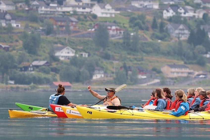 Un grupo de personas en un kayak amarillo sobre aguas tranquilas, con casas al fondo. 2