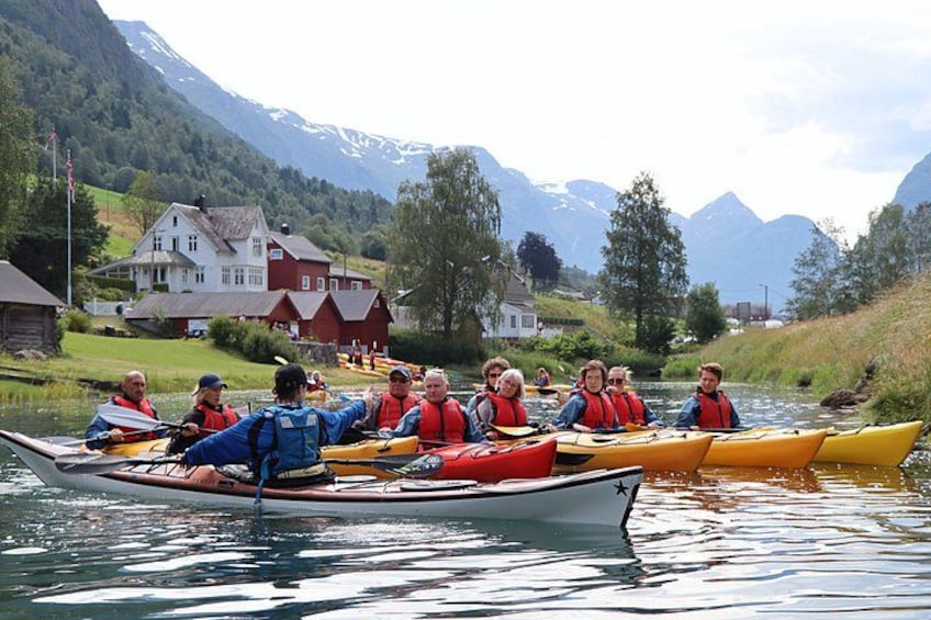 Un grupo de personas kayakendo en un río con casas y montañas al fondo. 5