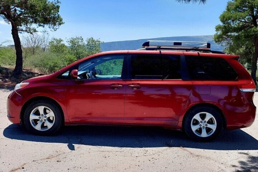 A red minivan parked on a dirt road with trees and a clear sky in the background. 4