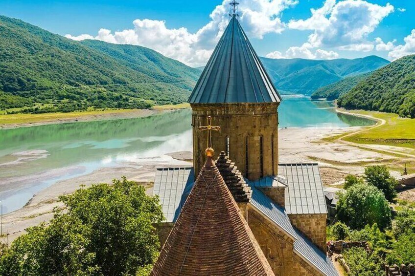 A church with a conical roof overlooking a river and mountains. 3