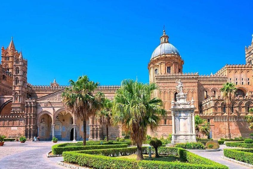 A historic building with intricate architecture, palm trees, and a statue in the foreground. 3