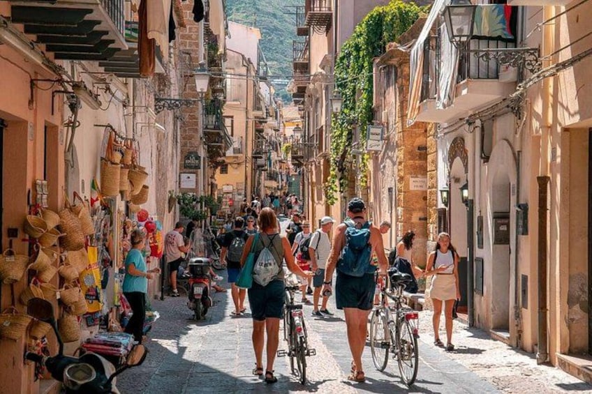 A narrow street lined with shops and buildings, with people walking and cycling. 1