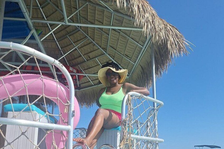 Una persona con traje de baño verde y sombrero de paja sentada en una silla bajo un tejado de paja. 2