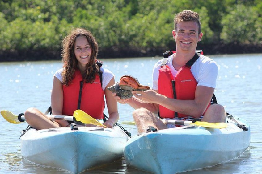 Two people in kayaks on a calm body of water with greenery in the background. 4