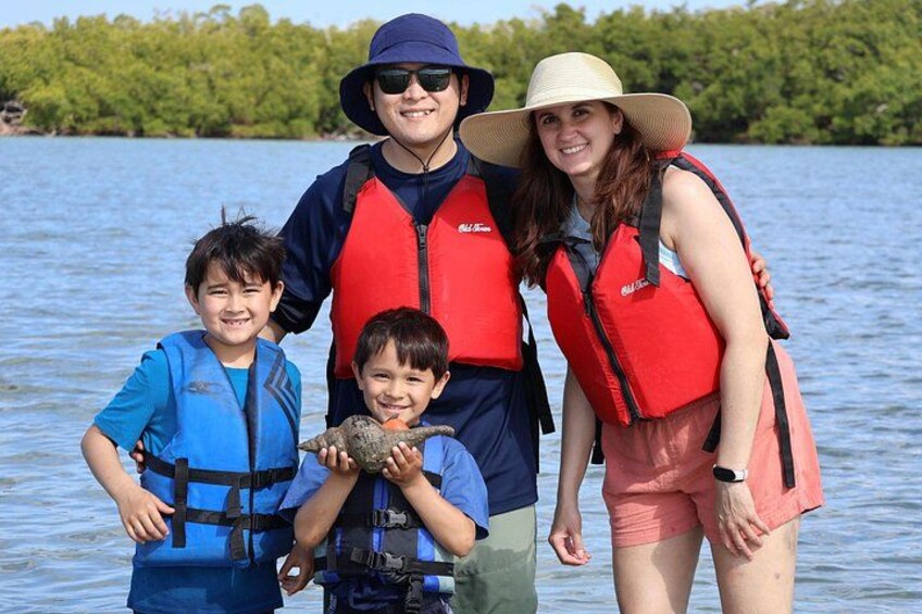 Una familia de cuatro personas con chalecos salvavidas, un niño sosteniendo una tortuga, y un lago con árboles al fondo. 3