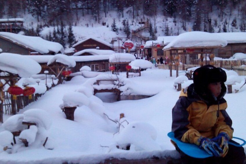A snowy landscape with a person on a snowboard, wooden buildings, and snow-covered trees. 4