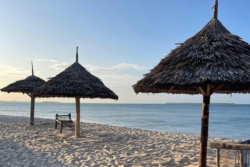 Ein Strand mit Reetsonnenstühlen und einer hölzernen Bank. 2
