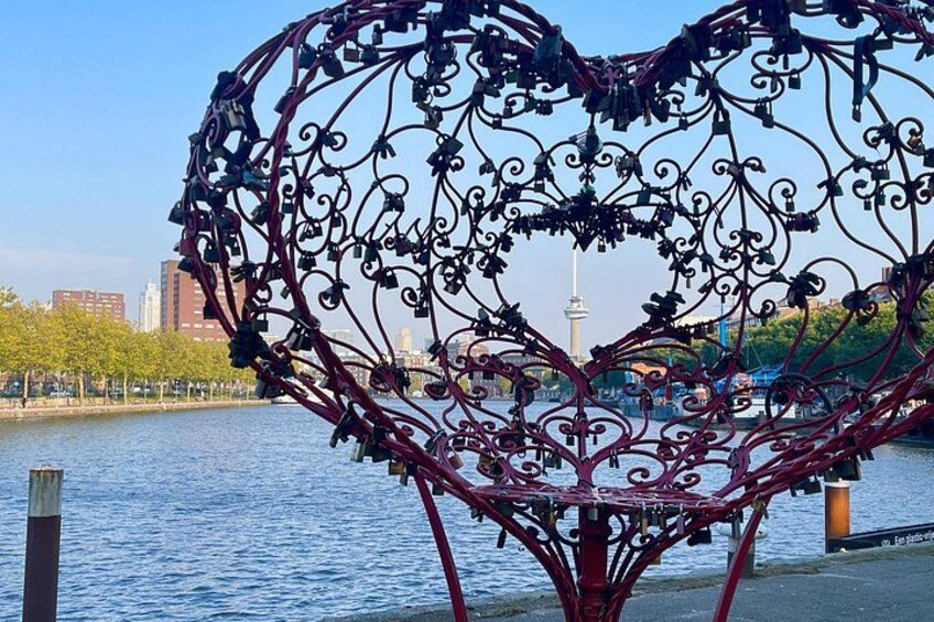 A heart-shaped metal sculpture by a waterfront with a cityscape in the background. 2