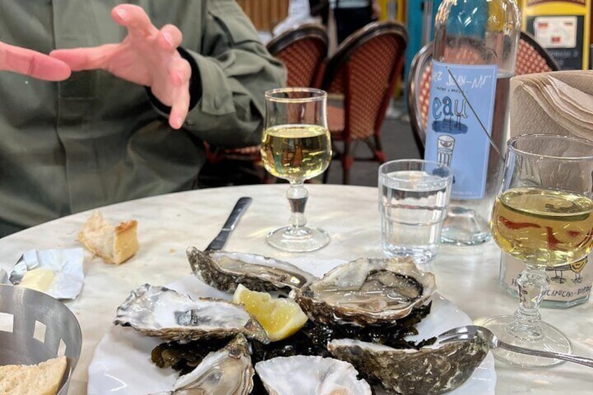 A table with oysters, glasses of white wine, and a bottle of eau de vie. 4