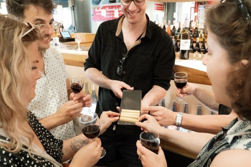 A group of people toasting with wine glasses, a man holding a tablet, and bottles of wine in the background. 4