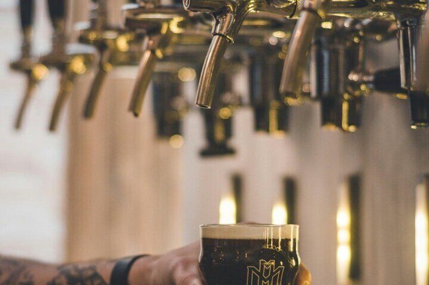 Une main tenant un verre de bière brune devant une rangée de robinets à bière. 4