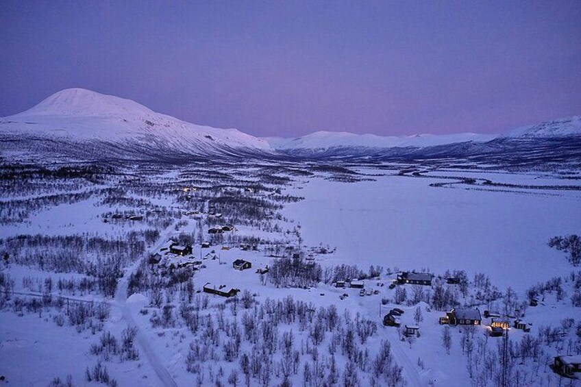 Ett snötäckt landskap med en liten bebyggelse och ett berg i bakgrunden. 2