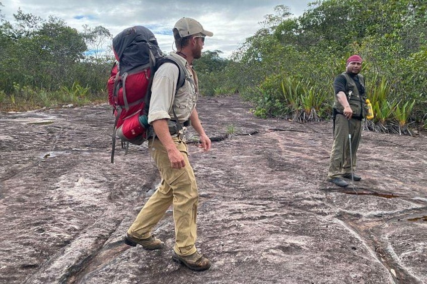 Two people hiking on a rocky terrain with vegetation in the background. 4