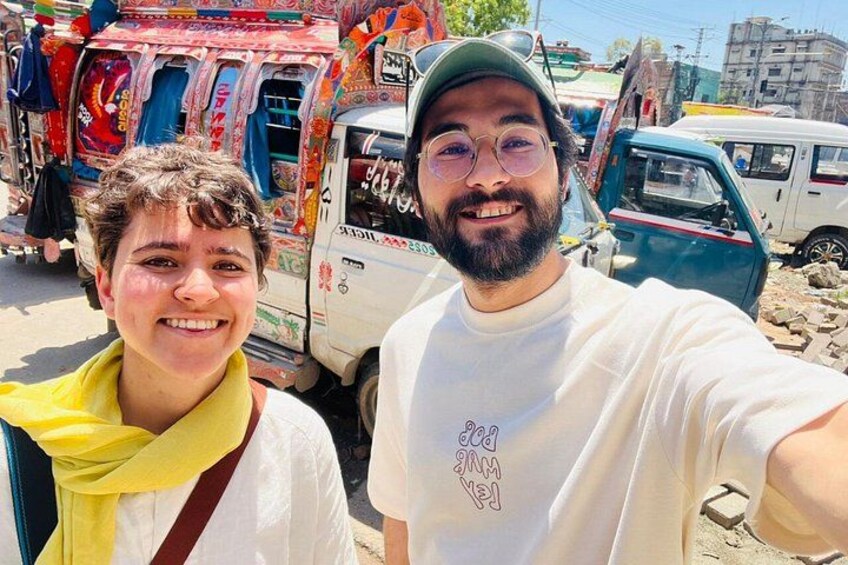 Two people taking a selfie with colorful vehicles and buildings in the background. 4
