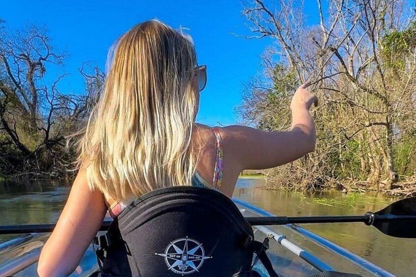 A person paddling a kayak on a river with trees and a clear sky in the background. 2