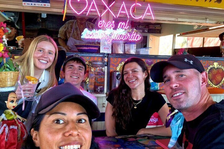 Un gruppo di persone presso una bancarella di cibo con un neon che recita 'CAJACA es mi especialidad'. 1