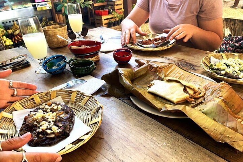 A wooden table with various dishes, including a plate with a stuffed meat dish, a basket with a wrapped food item, and several bowls. 1