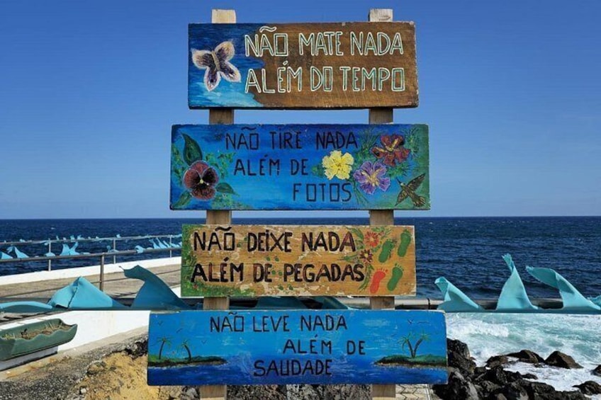 A beach with a wooden sign with multiple messages in Portuguese. 5